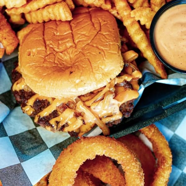 Slaw Burger's cheeseburger with grilled onions, crinkle fries, onion rings, and dipping sauce.