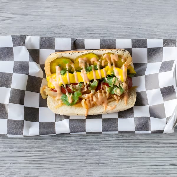 Slaw Burger's hot dog with pickles, mustard, and sauce on checkered paper.