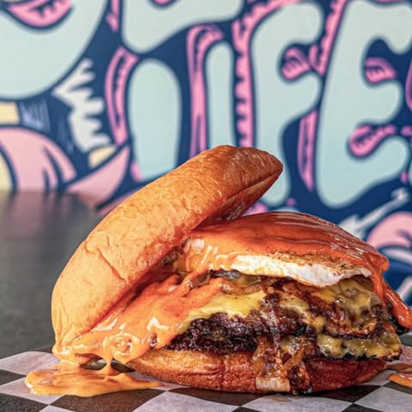 Slaw Burger's double patty burger with melted cheese, fried egg, and sauce on a checkered paper.