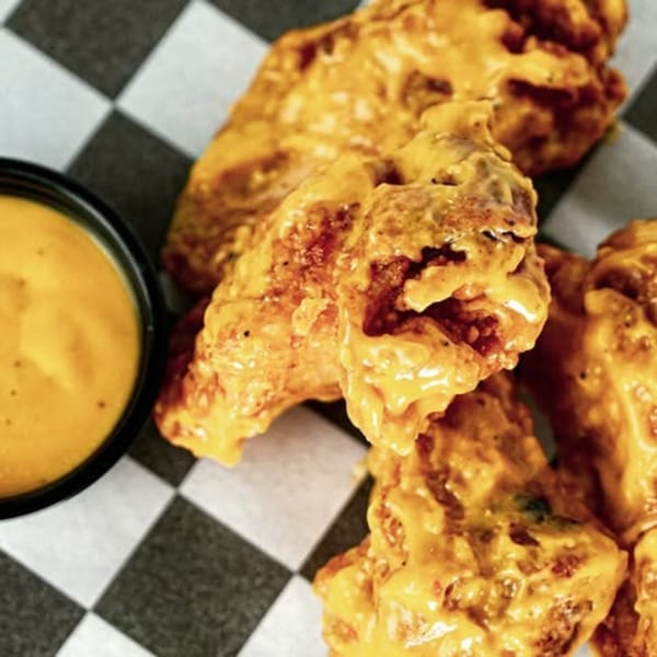 Crispy Slaw Burger chicken wings coated in a rich orange sauce, with a side of dipping sauce.