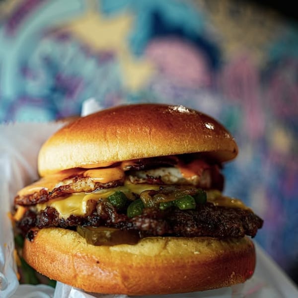 A Slaw Burger with a fried egg, melted cheese, jalapeños, and pickles on a brioche bun.