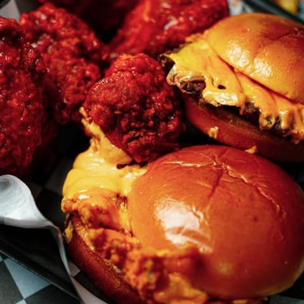 Two Slaw Burger cheeseburgers with melted cheese and a side of red hot wings.