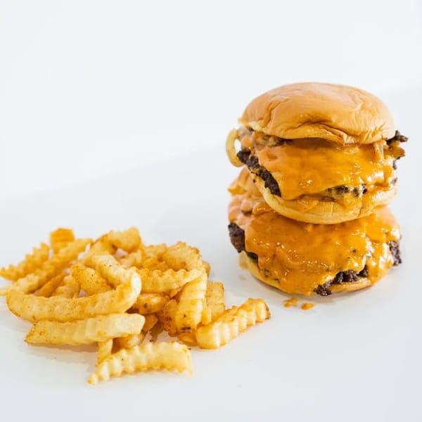 Two Slaw Burger cheeseburgers stacked with melted cheese and a side of crinkle-cut fries.