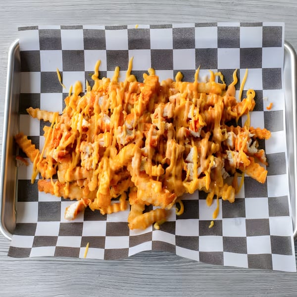 Slaw Burger's cheesy fries, topped with chicken pieces, served on checkered paper in a metal tray.