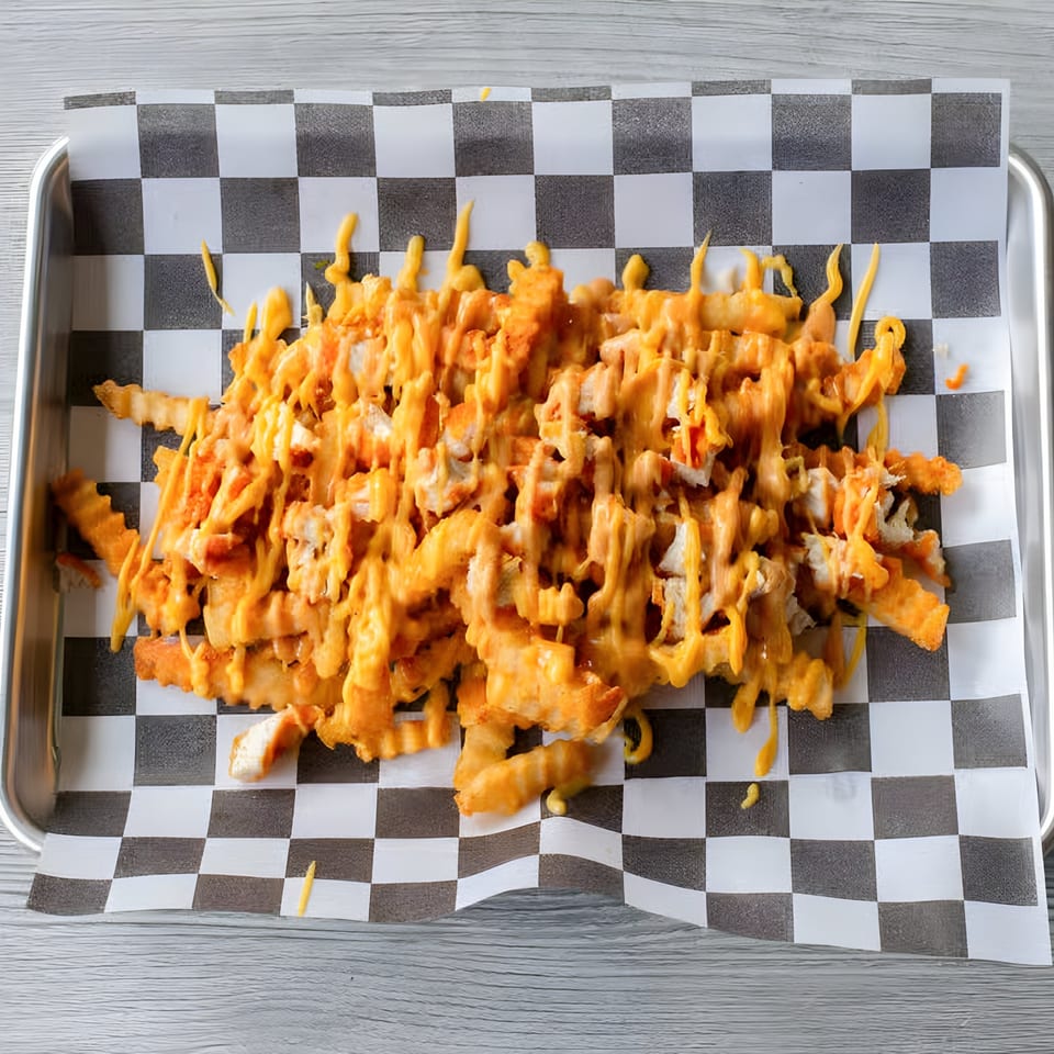 Slaw Burger's cheesy fries, topped with melted orange cheese and chicken pieces, on checkered paper.