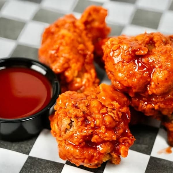 Three Slaw Burger hot wings with sauce, served on checkered paper with a side of dipping sauce.