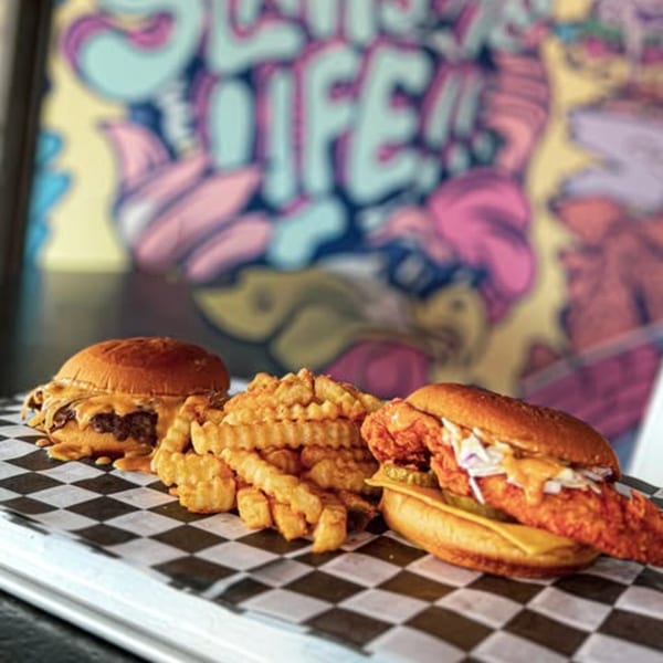 Slaw Burger's cheeseburger, chicken sandwich, and crinkle fries on checkered paper.