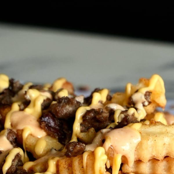 Close-up of Slaw Burger's crinkle-cut fries topped with ground beef, melted cheese, and sauce.