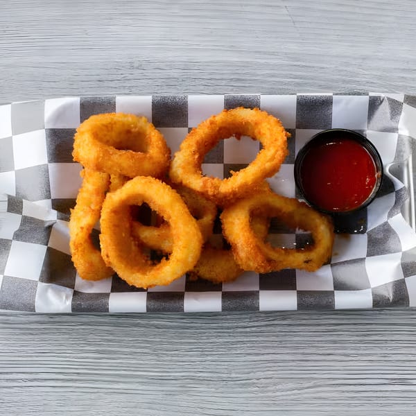 Golden-brown onion rings and a small cup of ketchup in a checkered paper tray on a wooden surface.